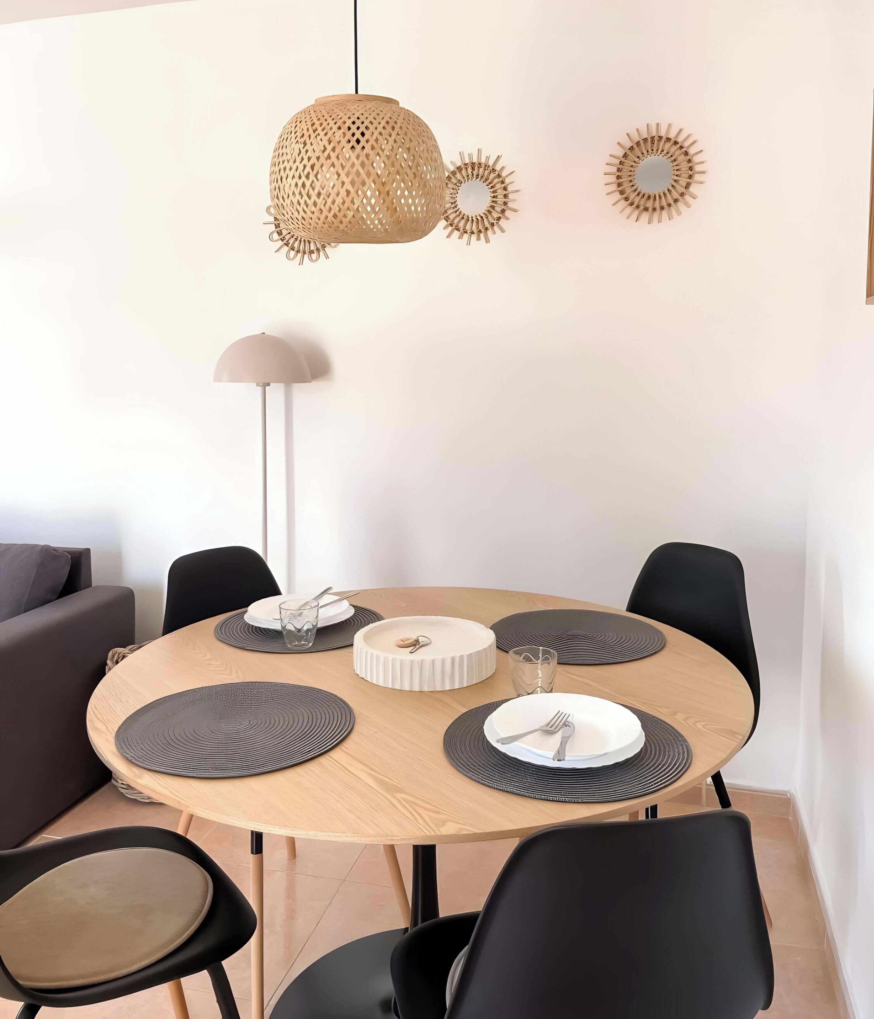Une table de salle à manger ronde, avec des chaises noires, une assiette blanche et un verre d’eau.