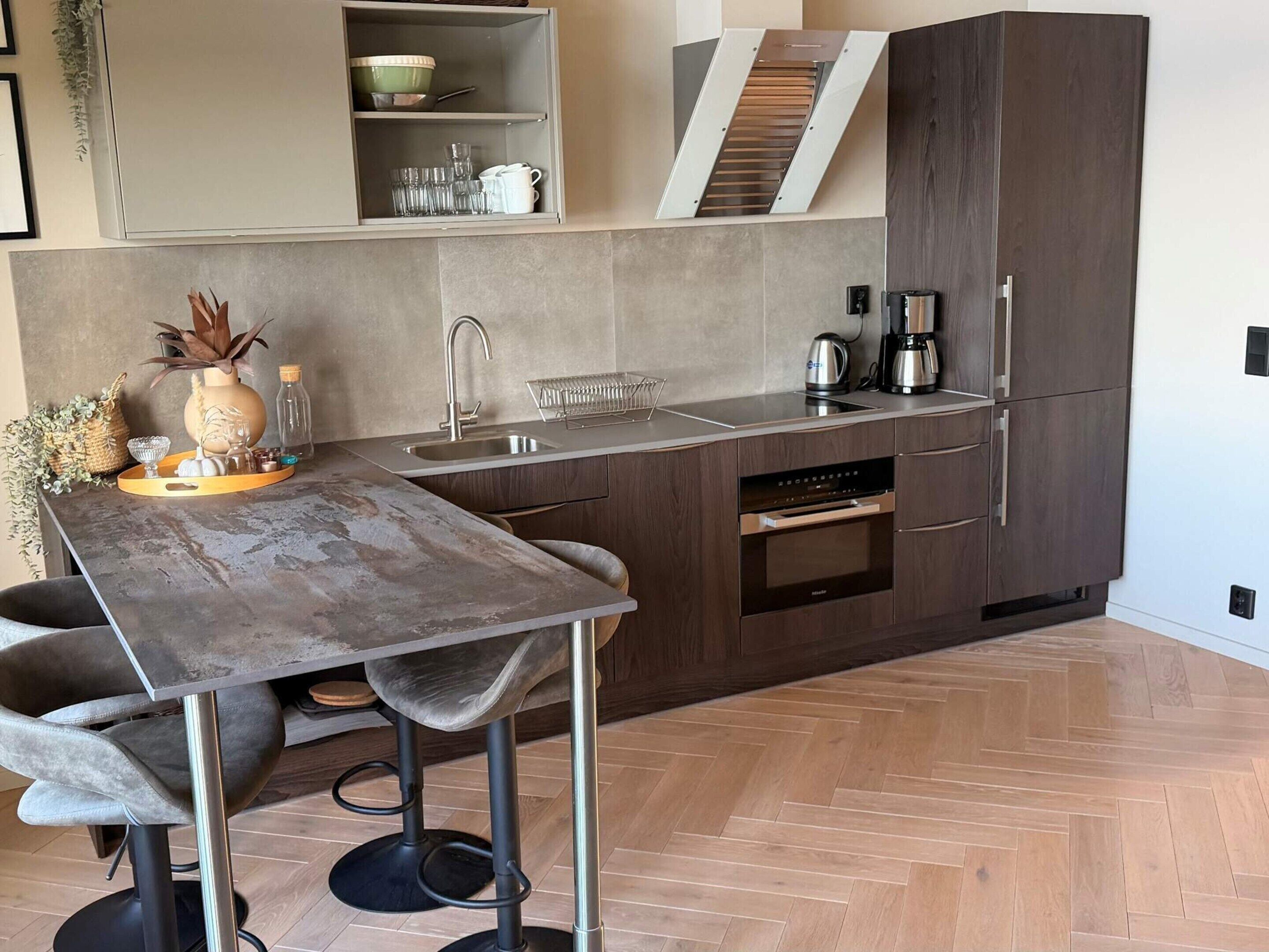 A modern kitchen with a central island, built-in oven, and a herringbone wood floor.