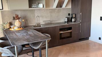 A modern kitchen with a central island, built-in oven, and a herringbone wood floor.