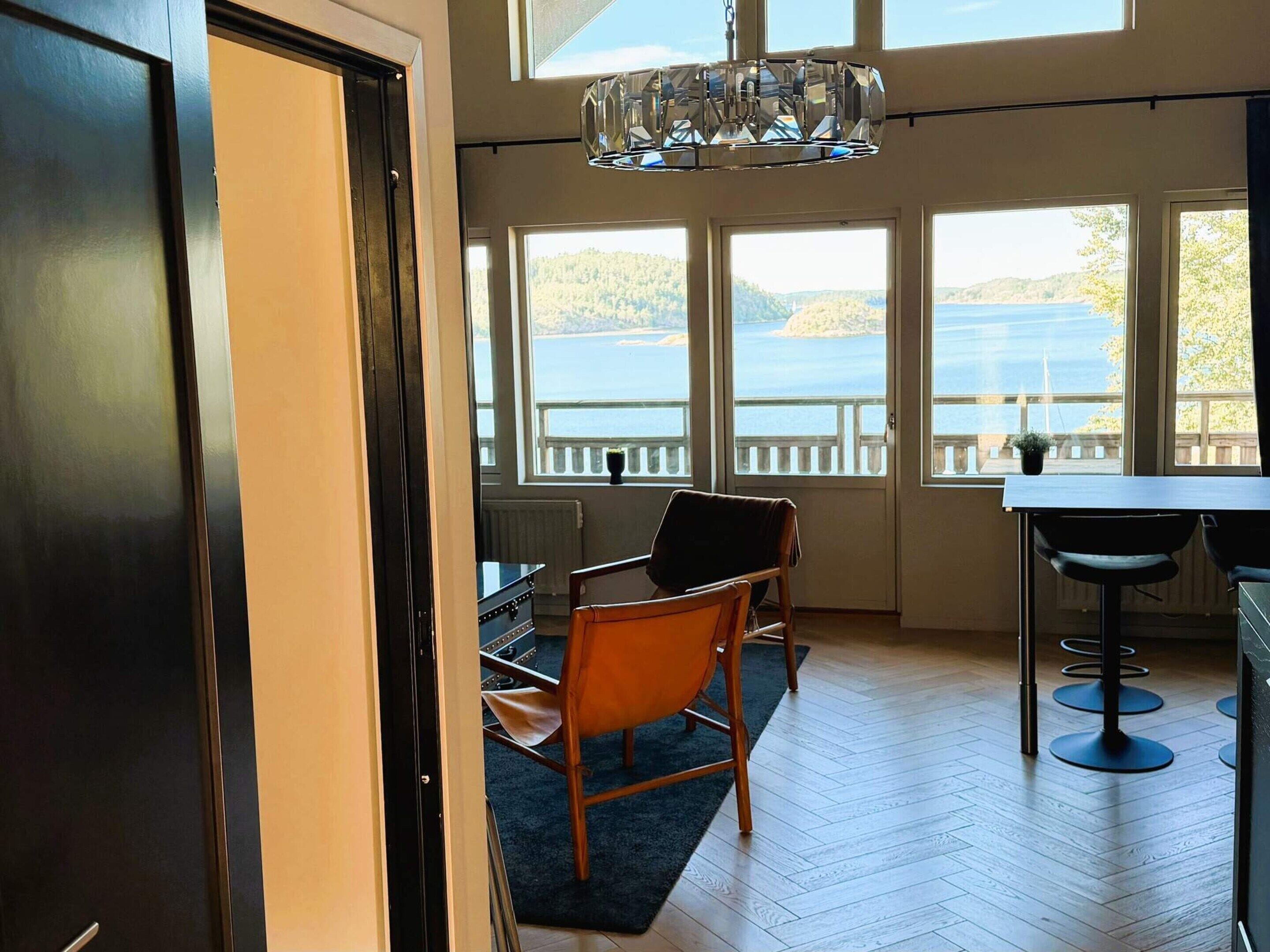 A room with a view of a lake, a wooden floor, a dining table, and a chair.