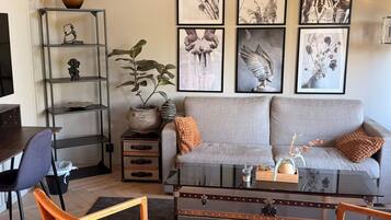 A living room with a grey sofa, a coffee table, a bookshelf, and a potted plant.