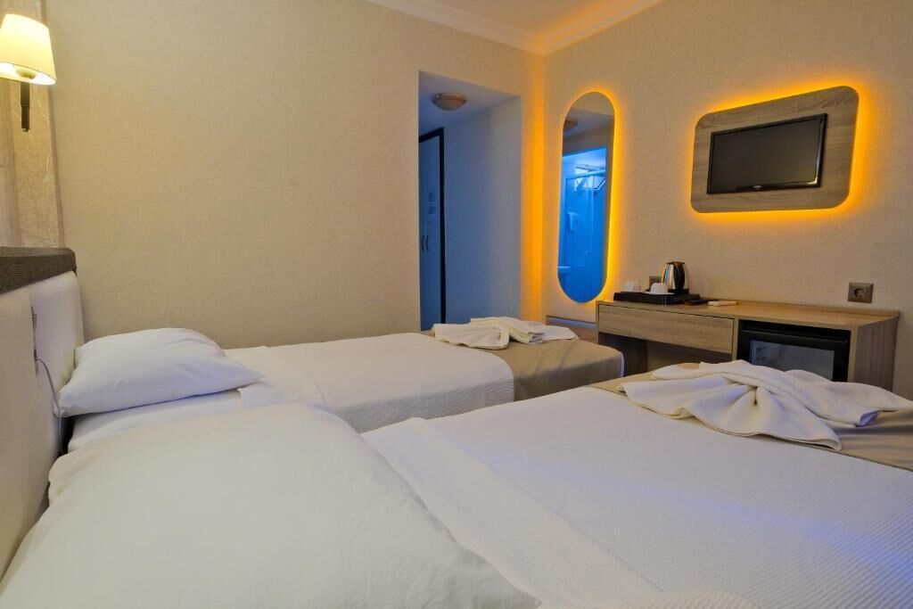 Quarto de hotel com duas camas, mesa de cabeceira, espelho e televisão na parede.