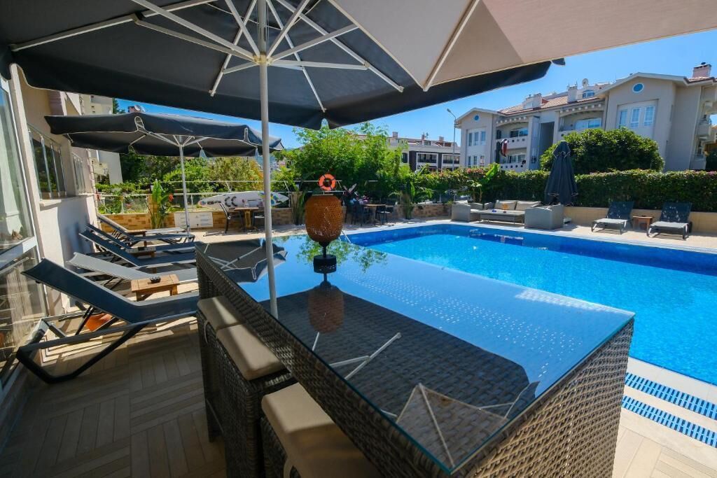 A swimming pool with lounge chairs and umbrellas, surrounded by buildings.