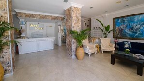 A hotel lobby with a reception desk, seating area, and a large painting. - MONİ HOTEL (Marmaris)