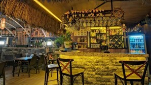 A bar area with a stone counter, wooden chairs, and a thatched ceiling. - MONİ HOTEL (Marmaris)