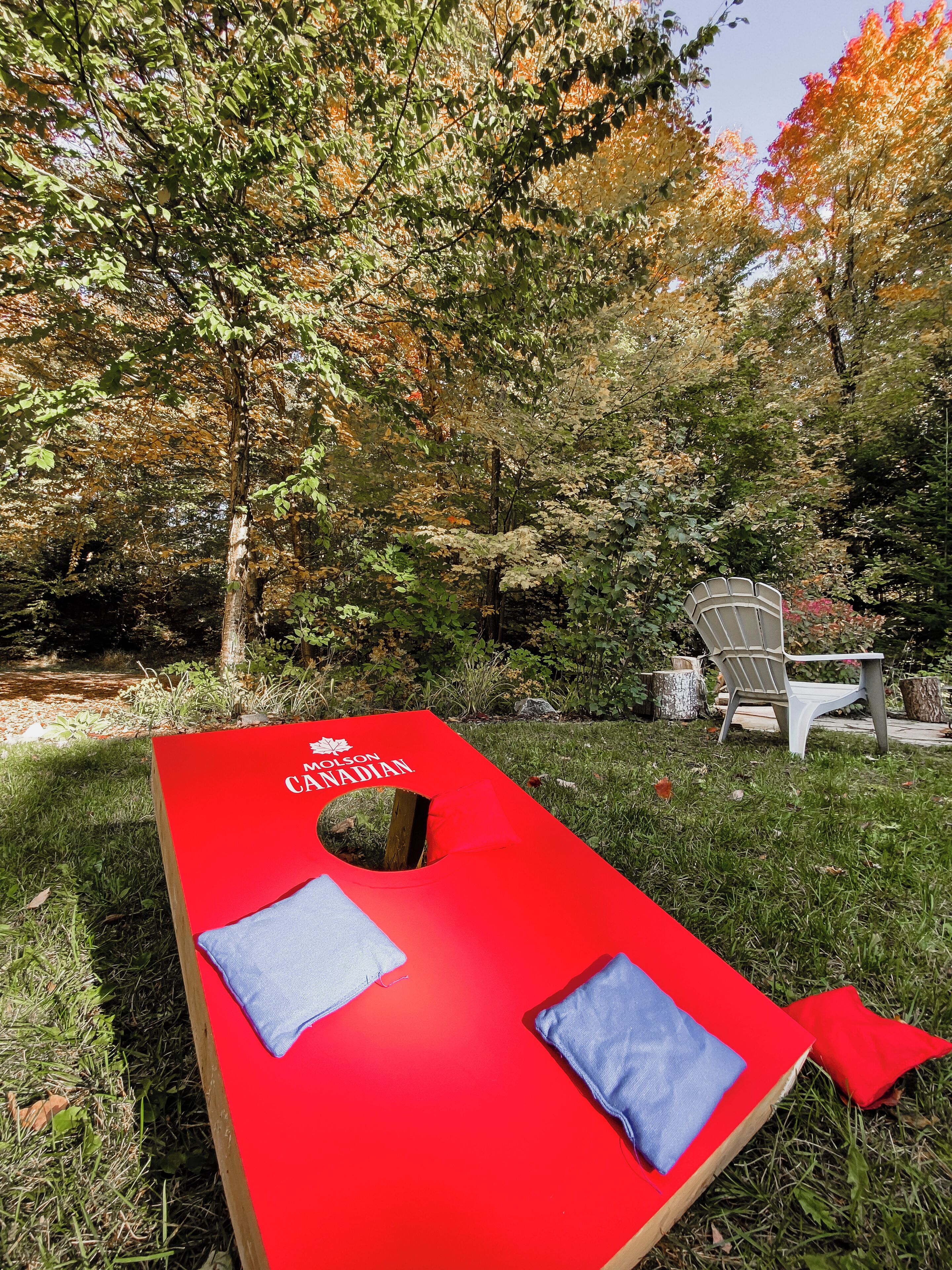 Une table de massage rouge, agrémentée de coussins, et une chaise, le tout dans un jardin arboré.