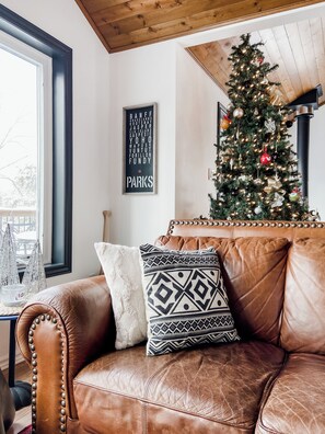 Ein Ledersofa mit dekorativen Kissen, ein Weihnachtsbaum und ein an der Wand befestigtes Schild.