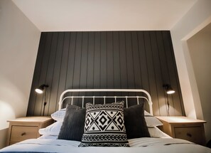 Een bed met een wit hoofdeinde, twee nachtkastjes en een wand met verticale panelen.