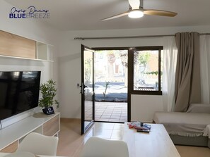 Un salon moderne doté d’un téléviseur à écran plat, d’un canapé, d’une table à manger et d’un ventilateur de plafond.