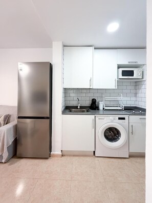 A modern kitchen with a stainless steel refrigerator, a microwave, and a built-in washing machine. - Oasis Dunas Blue Breeze Corralejo by B-Rent – Garden View Apartment (Corralejo)