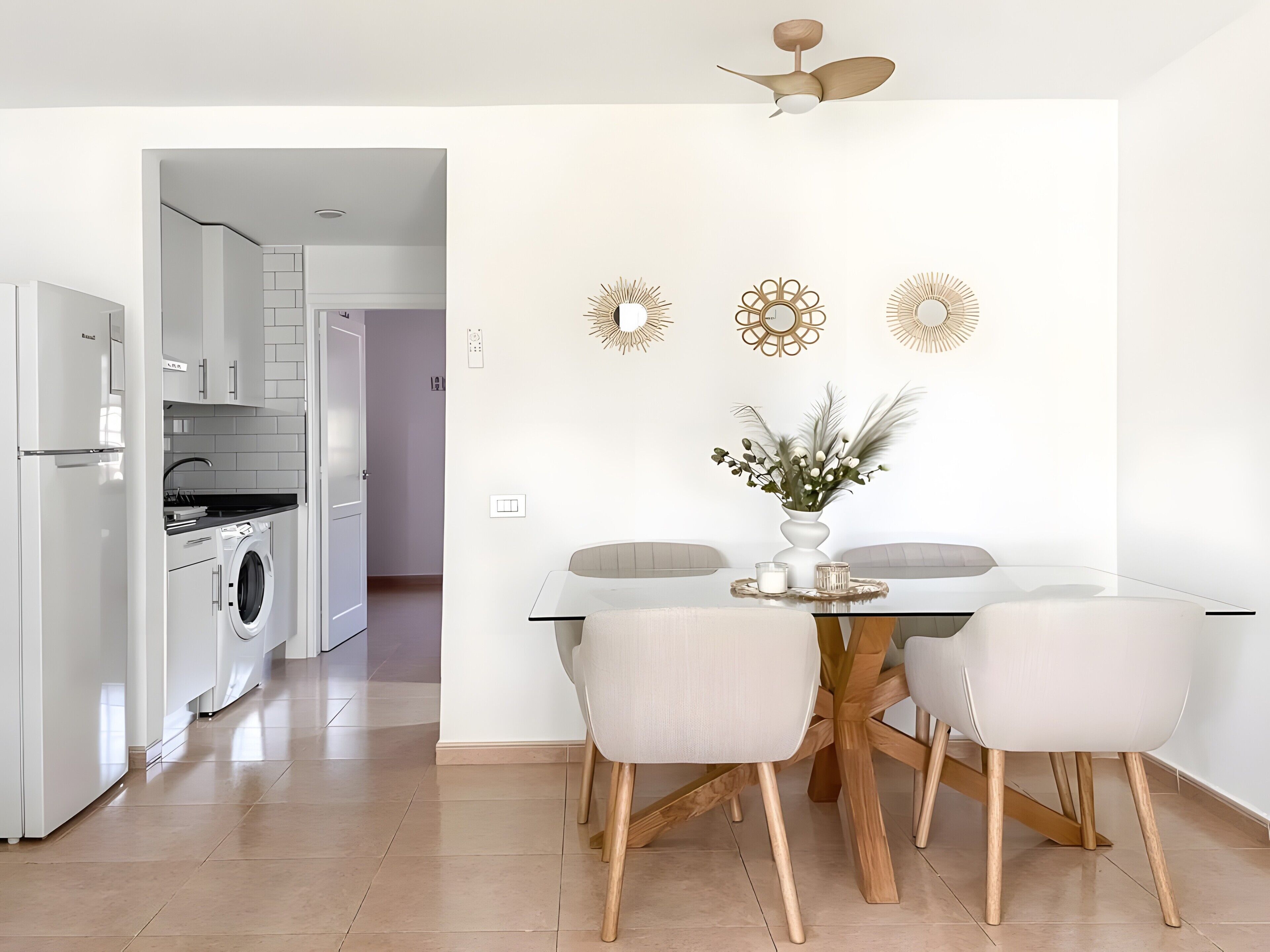 A modern kitchen with a built-in washing machine, a dining area with a glass table and wooden chairs, and decorative wall art.