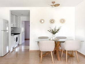 A modern kitchen with a built-in washing machine, a dining area with a glass table and wooden chairs, and decorative wall art. - Oasis Dunas 406 near the pool by B-Rent (Corralejo)