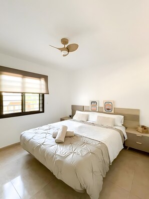 A bedroom with a bed, a nightstand, a ceiling fan, a window with blinds, and a wall with a framed picture. - Oasis Dunas 406 near the pool by B-Rent (Corralejo)