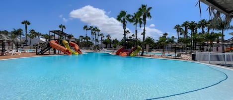Una piscina grande con varias toboganes, rodeada de palmeras y sillas de descanso.