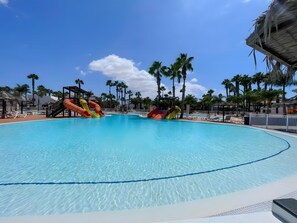 A large swimming pool with multiple slides, surrounded by palm trees and lounge chairs. - Oasis Dunas 406 near the pool by B-Rent (Corralejo)