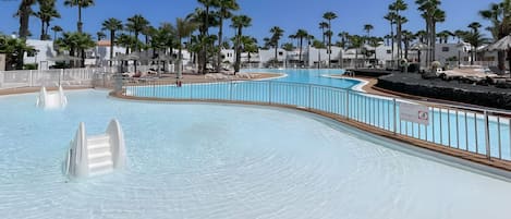Une piscine au design incurvé, entourée de palmiers et d’une clôture blanche.