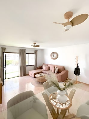 A modern living room with a sectional sofa, a dining table with chairs, a ceiling fan, and a large window with curtains. - Oasis Dunas 406 near the pool by B-Rent (Corralejo)
