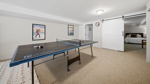 Quarto com mesa de pingue-pongue, cama e porta que dá para outro espaço.