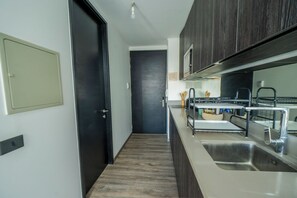 A modern kitchen with a stainless steel sink, dark wooden cabinets, and a light-colored countertop. - Executive Office · Gym · Coworking Space · Cumming Metro Station (Santiago)