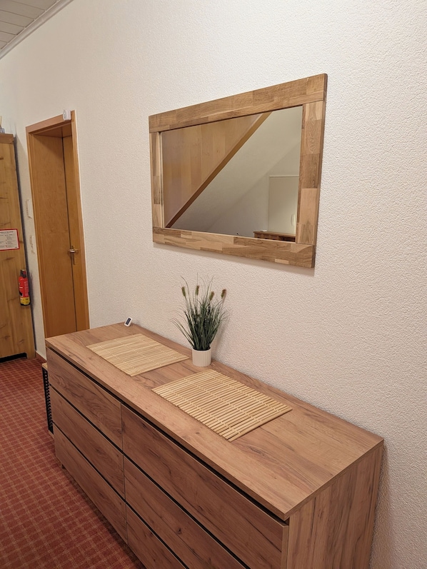 Une coiffeuse en bois avec un miroir au-dessus, une petite plante en pot et un tapis à carreaux posé sur le comptoir.