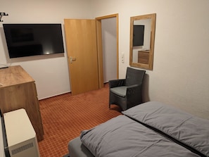 Une pièce comprenant un lit, une chaise, un téléviseur et un bureau en bois.