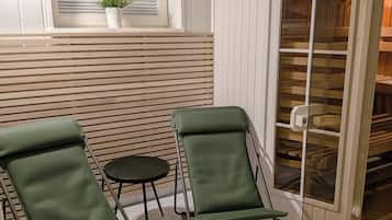 Ein Zimmer mit zwei grünen Lounge-Sesseln, einem kleinen runden Tisch, einem Fenster mit Jalousien und einem weißen Schrank mit Glastüren.