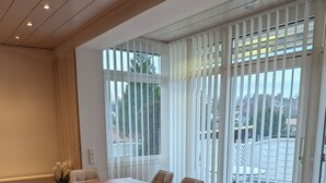 A conference room with a long table, chairs, a bench, and large windows with blinds.