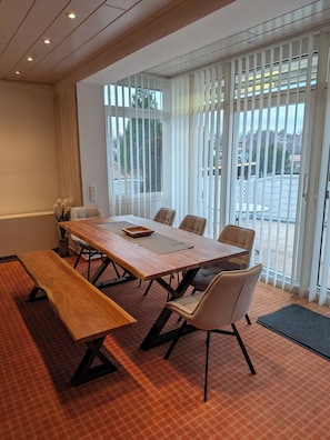A conference room with a long table, chairs, a bench, and large windows with blinds.