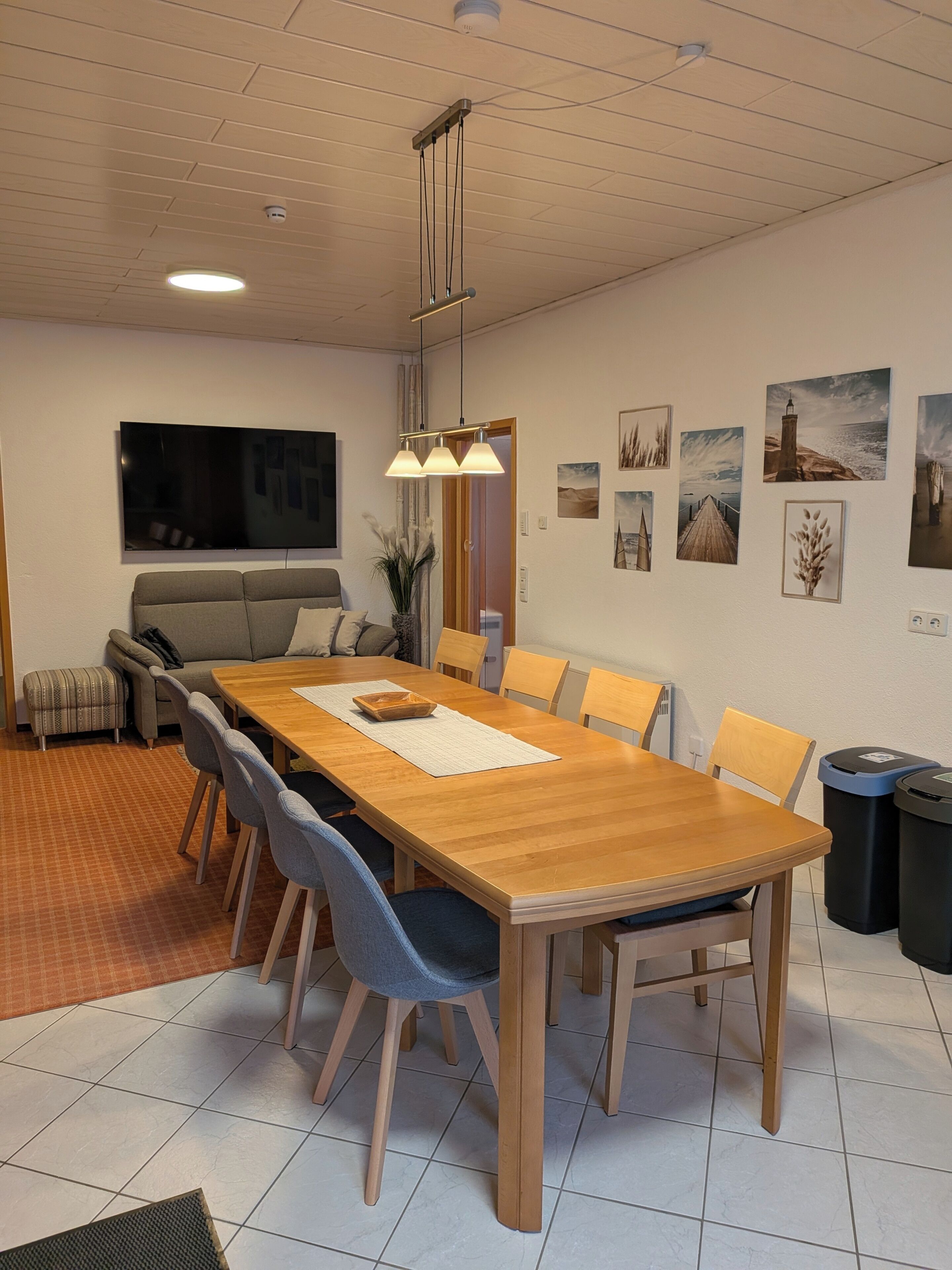 Ein Essbereich mit Holztisch, Stühlen, einer Couch, einem Fernseher und Wandbildern.