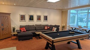 A modern living room with a pool table, a sectional sofa, and a dining area with a table and chairs.
