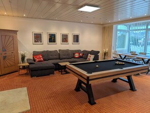 A modern living room with a pool table, a sectional sofa, and a dining area with a table and chairs.