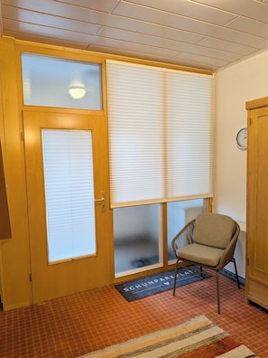 A room with a wooden door, frosted glass panels, a chair, a clock on the wall, and a doormat.