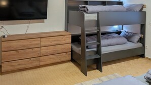 A bunk bed with a TV mounted on the wall, a wooden dresser, and a lamp.