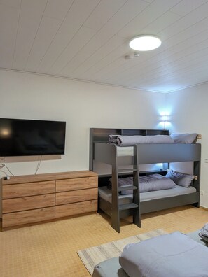 A bunk bed with a TV mounted on the wall, a wooden dresser, and a lamp.
