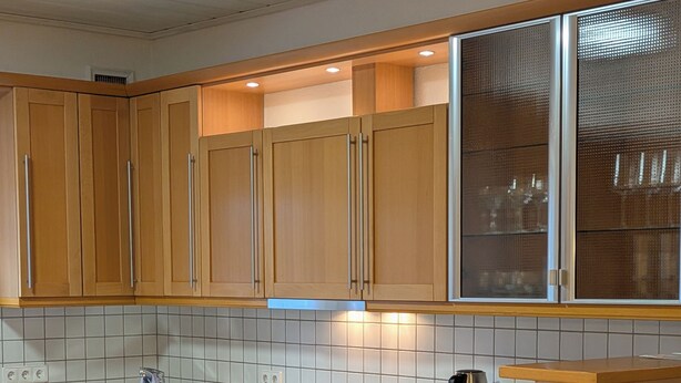 A modern kitchen with wooden cabinets, a built-in oven, a coffee maker, and a dining area with a table and chairs.