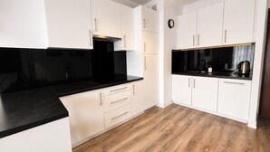 Cozinha moderna com armários brancos, bancada preta e piso de madeira.