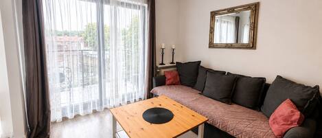 A living room with a sofa, a wooden coffee table, a mirror, and a window with curtains.
