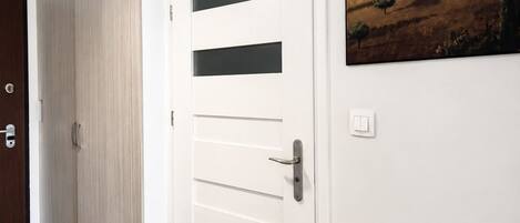 Un couloir avec une porte blanche, une armoire en bois et un tableau représentant une maison accroché au mur.