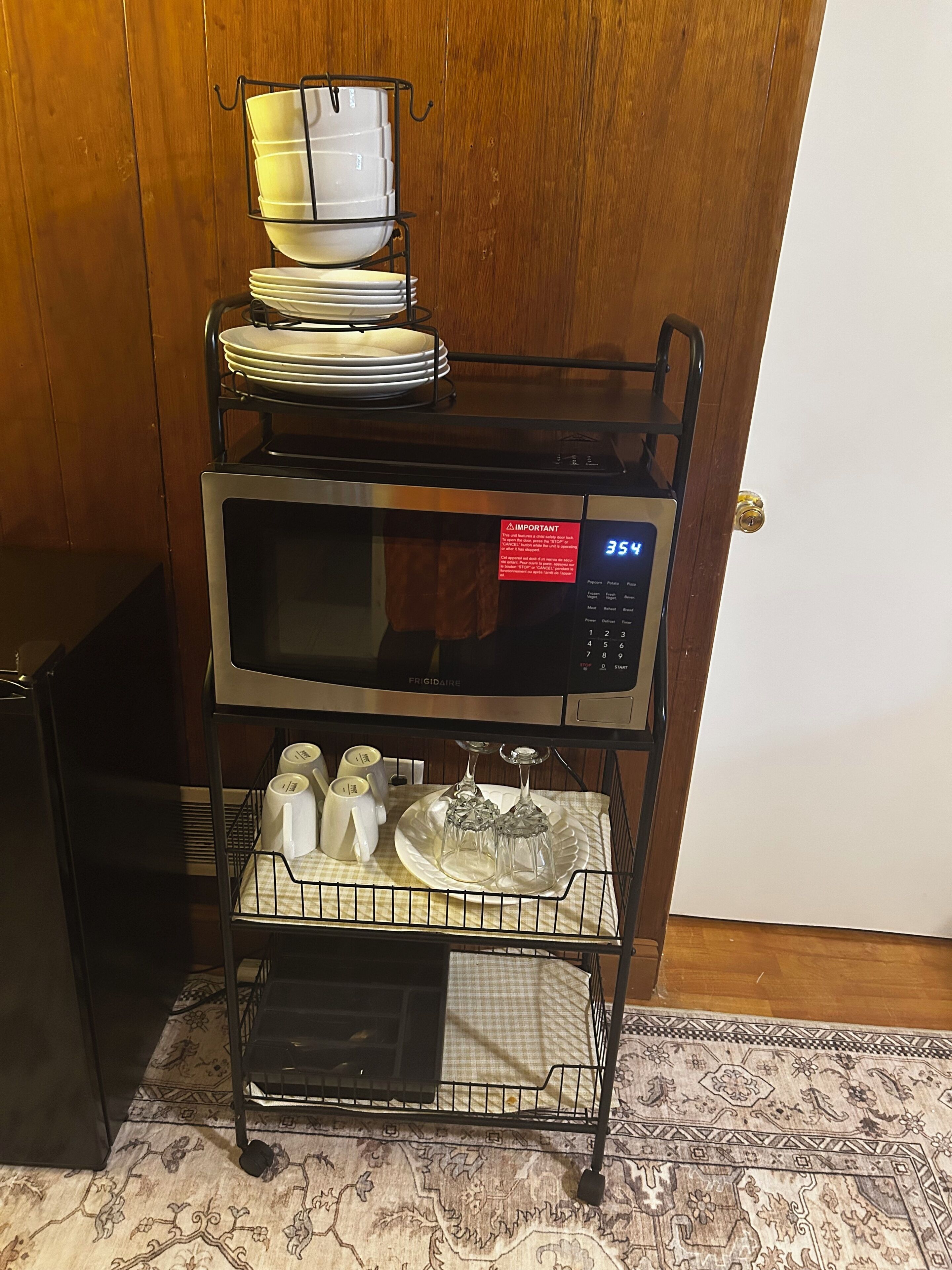 A kitchen cart with a microwave, stacked dishes, and utensils.