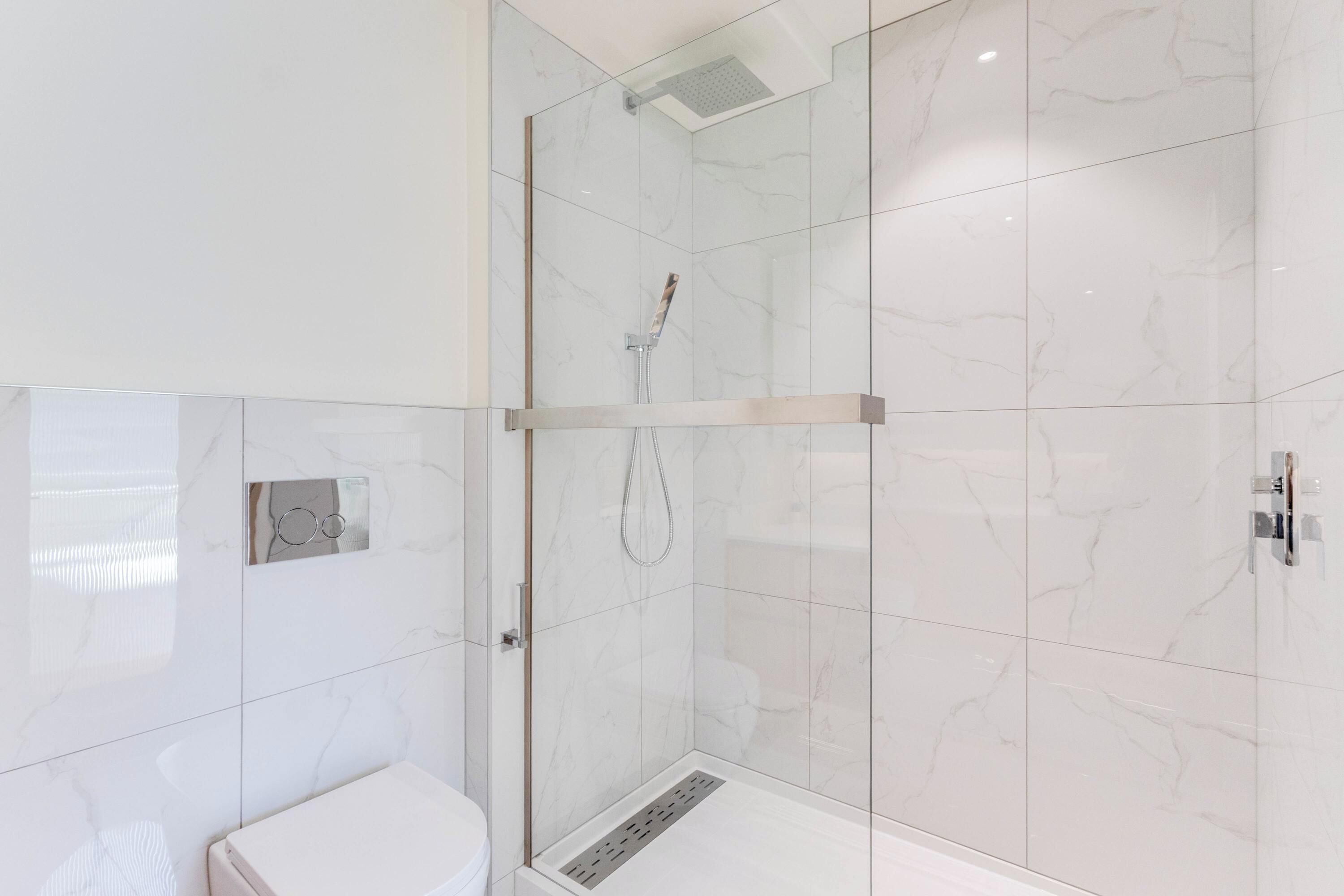 A modern bathroom with a glass-enclosed shower, white marble tiles, and a visible toilet.