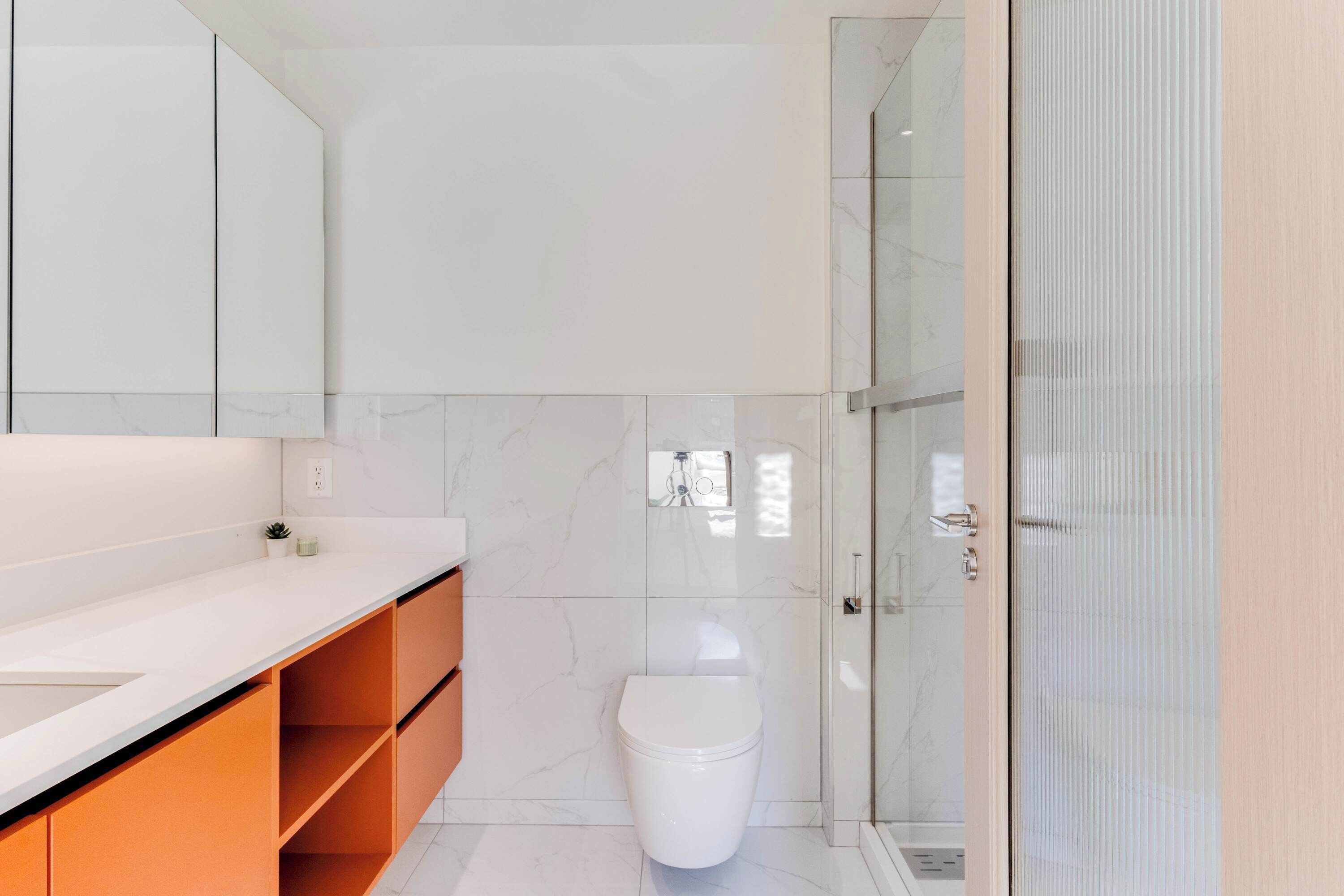 Un bagno moderno con il water bianco, un box doccia in vetro e un mobile lavabo con piano in marmo.