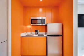 Una cocina compacta con microondas y refrigerador, un lavamanos y una cafetera.