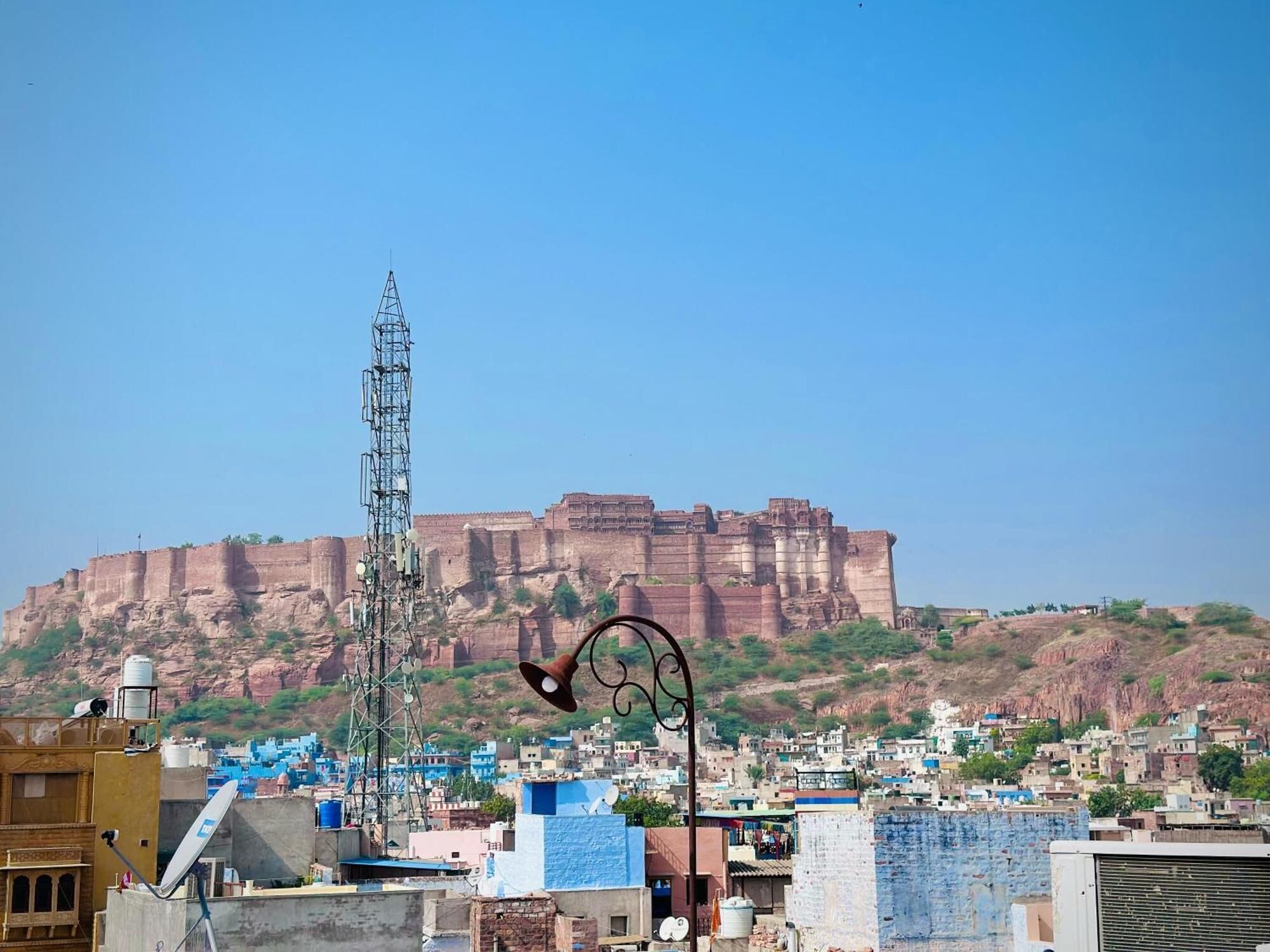 A cityscape with a prominent historical fort in the background and a tall communication tower in the foreground.