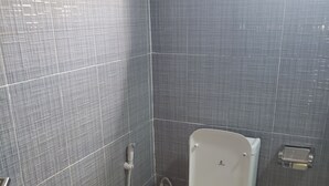 Un baño con inodoro blanco, paredes con azulejos grises y una tubería a la vista.