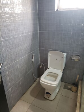 A bathroom with a white toilet, grey tiled walls, and a visible pipe on the wall.