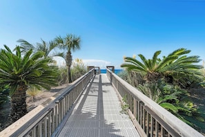 A wooden boardwalk leading to a beach with palm trees and a clear blue sky. - The Crescent 403 (Miramar Beach)