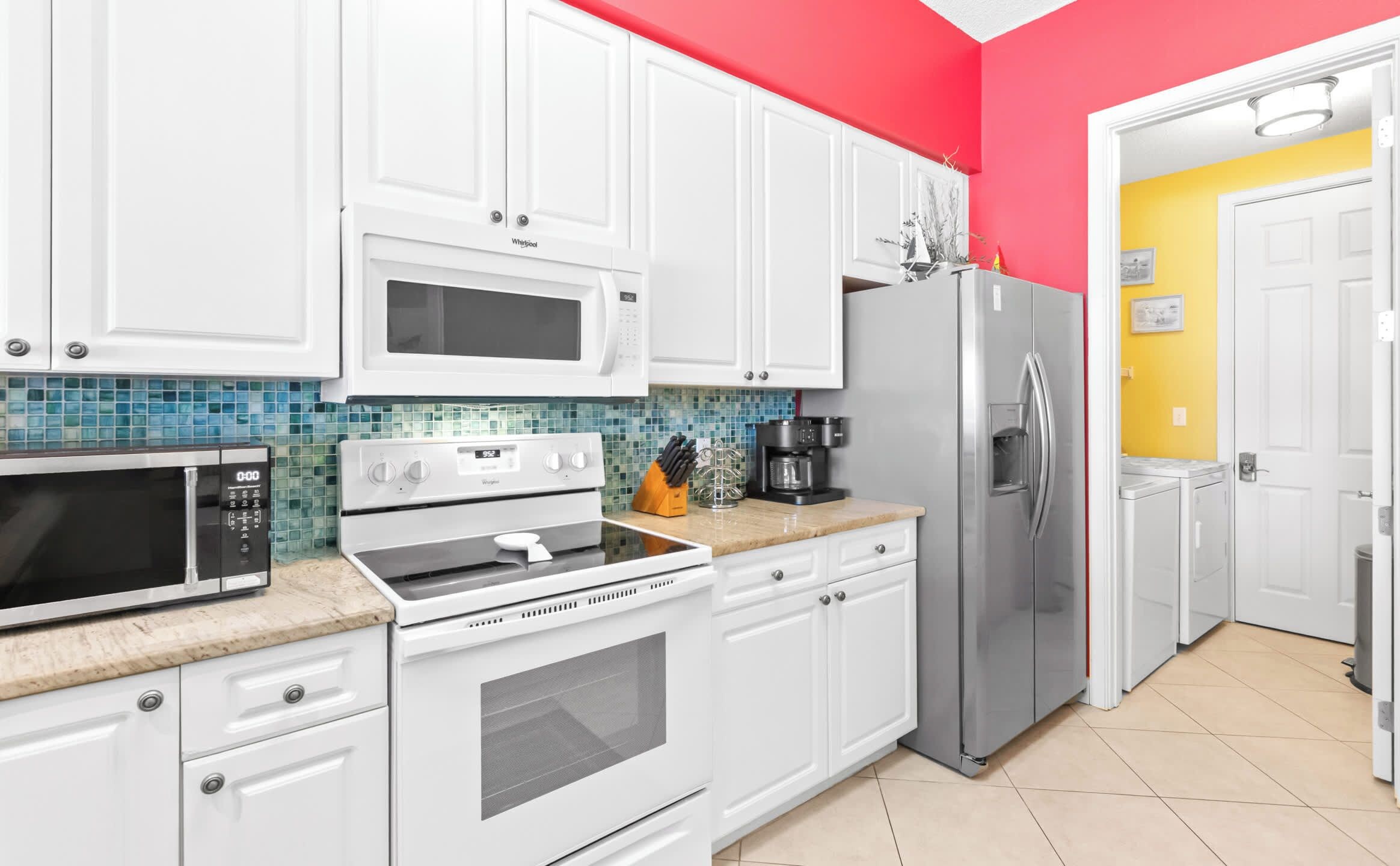 Una cocina con armarios blancos, microondas, horno, refrigerador y cafetera.