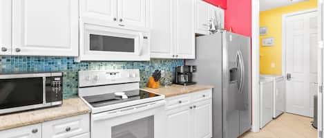 Una cocina con armarios blancos, microondas, horno, refrigerador y cafetera.