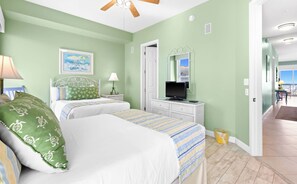 A bedroom with two beds, a television, a ceiling fan, and a painting on the wall. - The Crescent 403 (Miramar Beach)