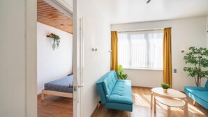 A modern, well-lit room with a wooden ceiling, a blue sofa, a small round table, and a window with yellow curtains.